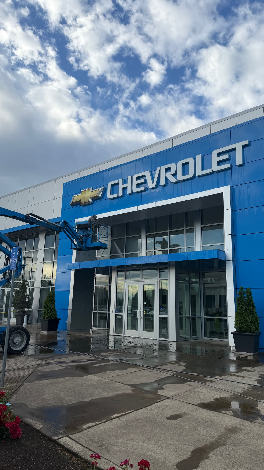 Technician washing a Chevrolet dealership exterior from a boom lift