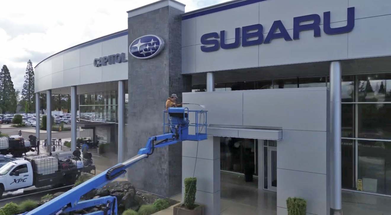 Technician washing a Subaru dealership exterior from a boom lift