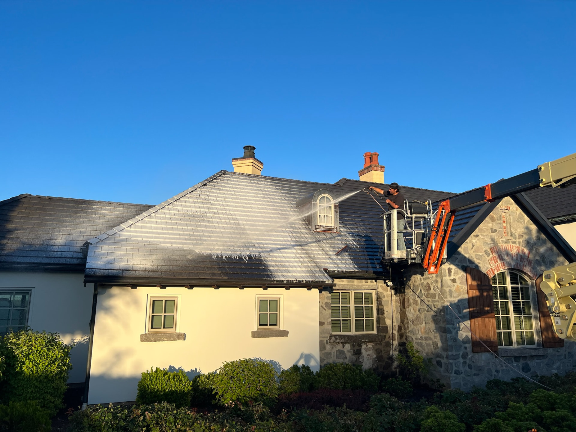 Technician on a lift soft washing a slate roof on a custom home