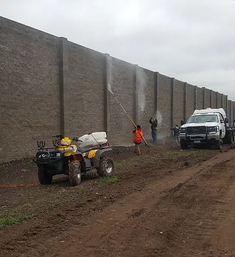 Crew soft washing a tall concrete retaining wall on site
